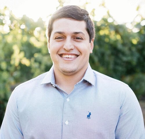 Smiling young man outdoors in natural light, wearing a light blue shirt, representing friendliness and approachability.