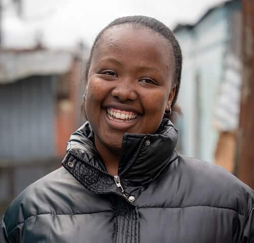 Smiling woman outdoors wearing black jacket, urban background, showcasing positivity and warmth.
