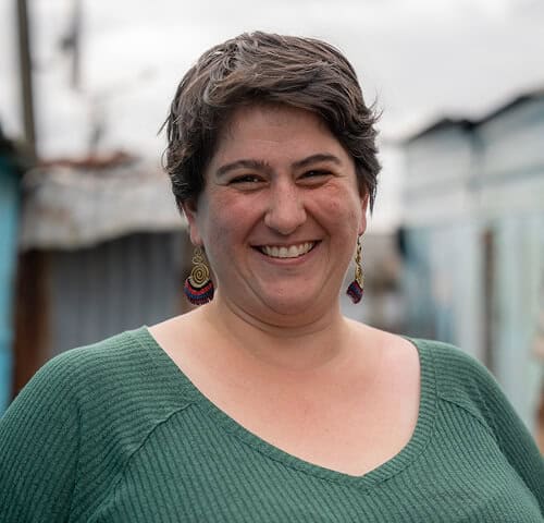 Smiling woman with short dark hair wearing a green sweater outdoors, showcasing friendliness and confidence.