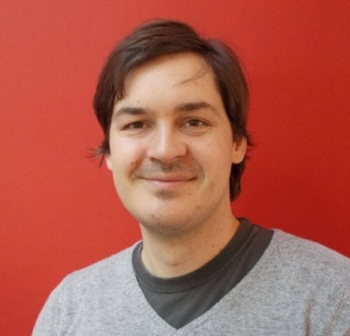 Friendly professional man smiling against red background, representing warmth and approachability.