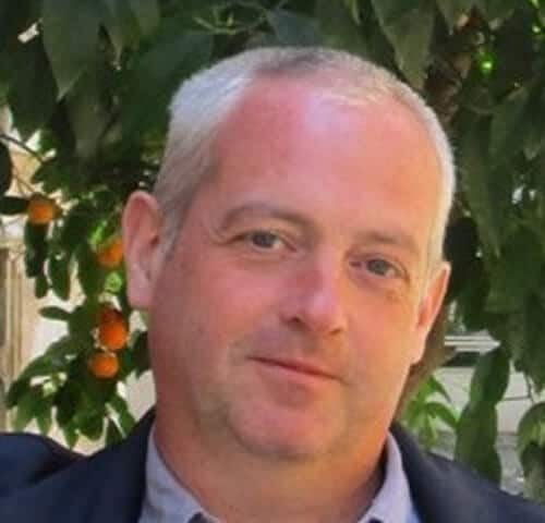 Close-up of a man outdoors with orange trees in the background, during daytime.