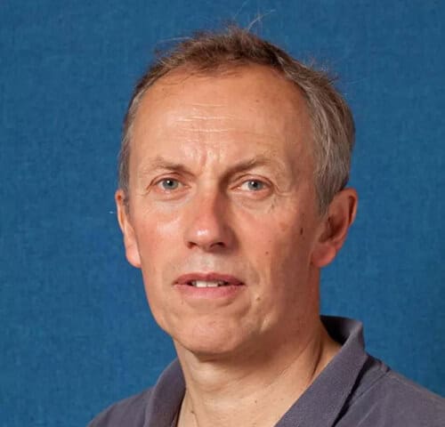 A middle-aged man with short, light hair against a blue background.