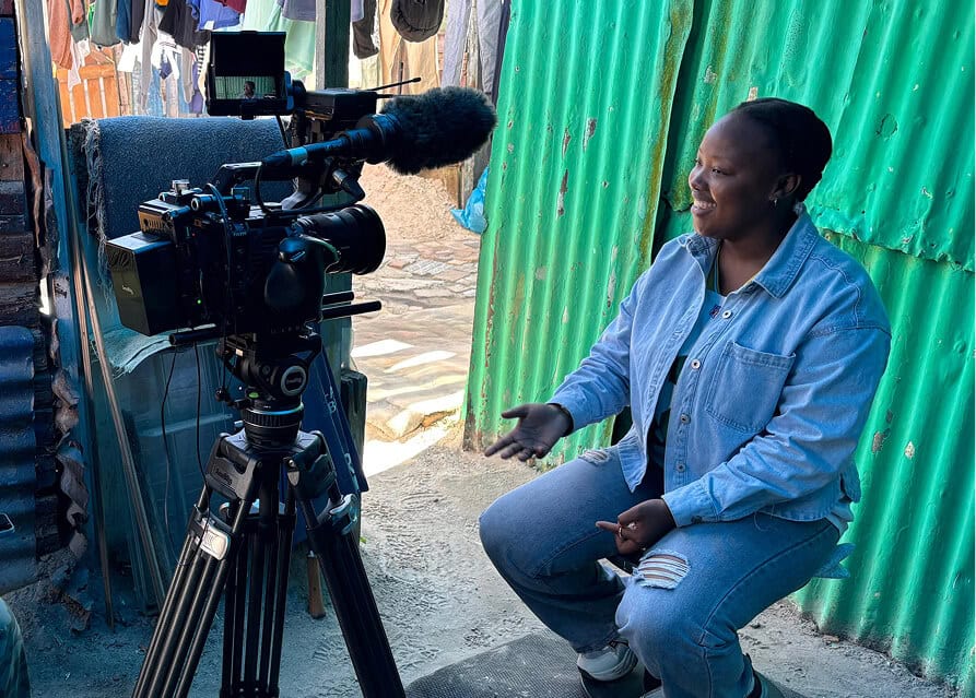 Woman being interviewed outdoors with a professional camera setup in a rustic setting.
