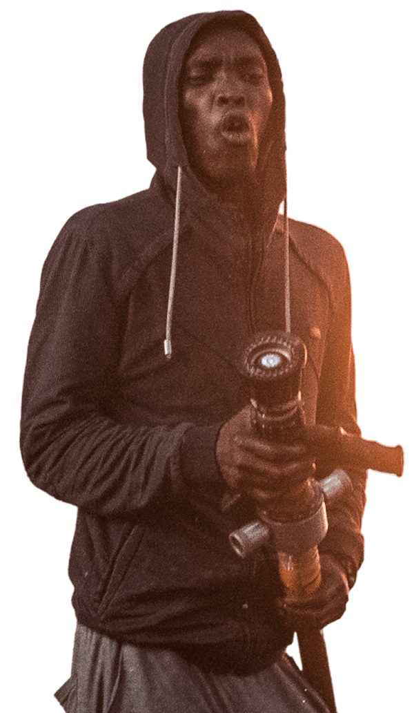 A person in a hoodie holding a jet torch with a focused expression at night.