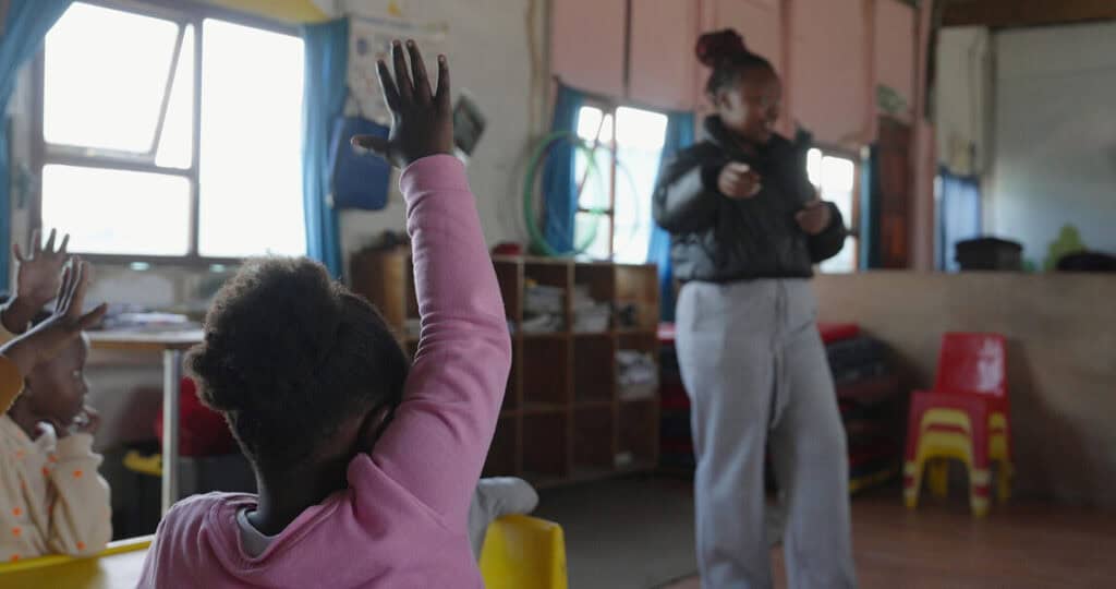 Engaged children raising hands in classroom with teacher during educational activity.