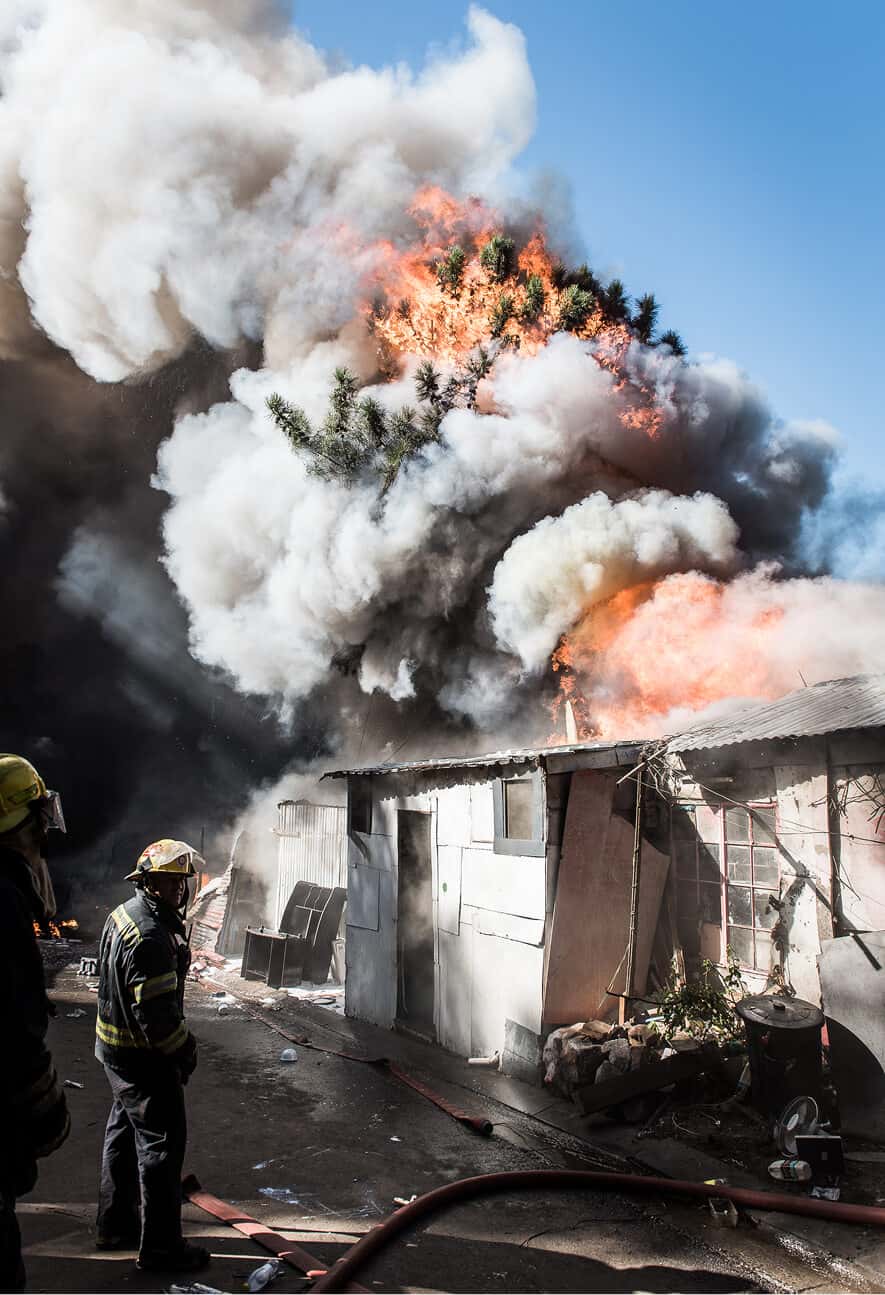 Fire outbreak engulfing a house with thick smoke and flames, firefighters battling the blaze.