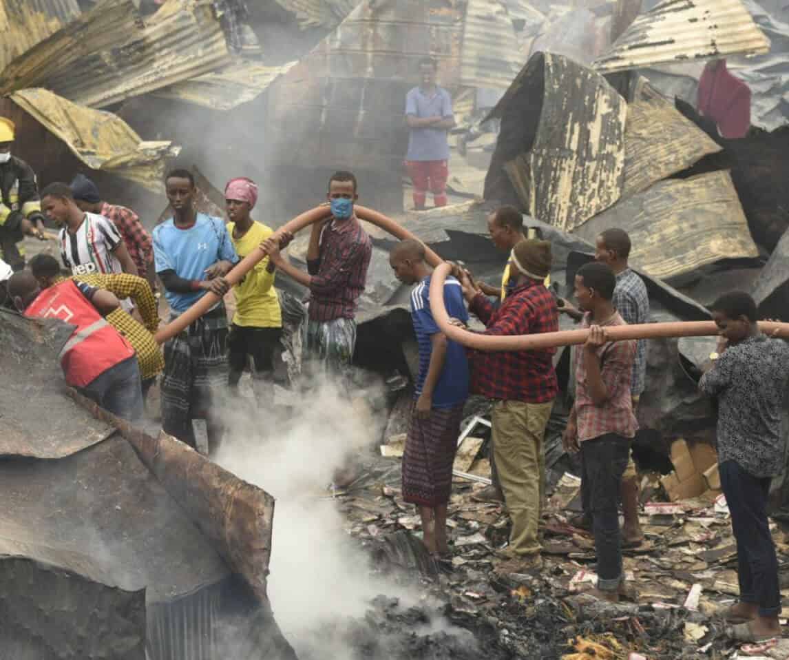 Collapsed building fire rescue in aftermath of destruction, community helping firefighters to extinguish flames.