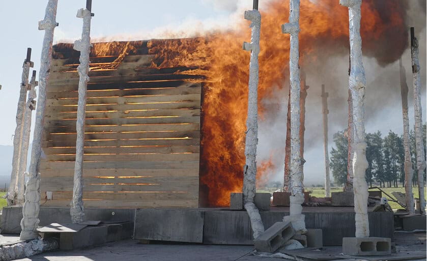 Charred wooden structure on fire with smoke and burning flames.