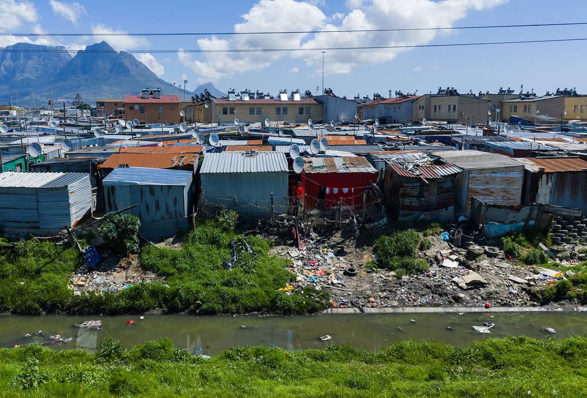 Makeshift housing with corrugated metal roofs and satellite dishes in a poverty-stricken area.